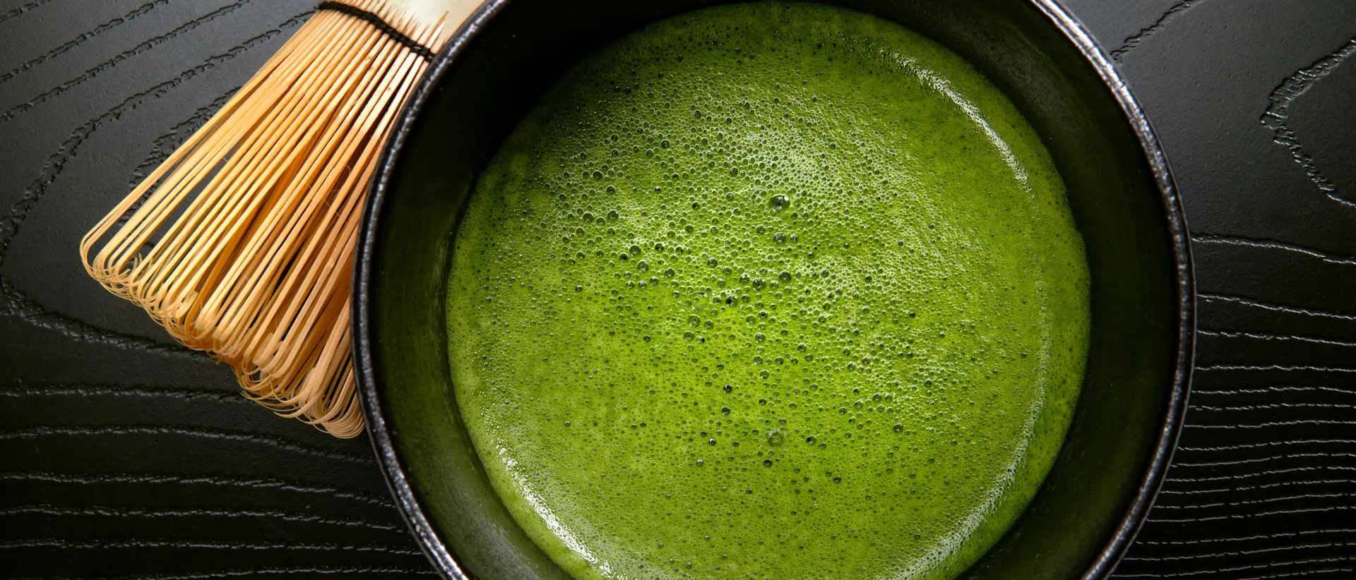 Stone-milled Japanese matcha, freshly whisked in a black tea bowl with a bamboo chasen, on dark wood — Nagamine Seicha, Yaizu, Shizuoka